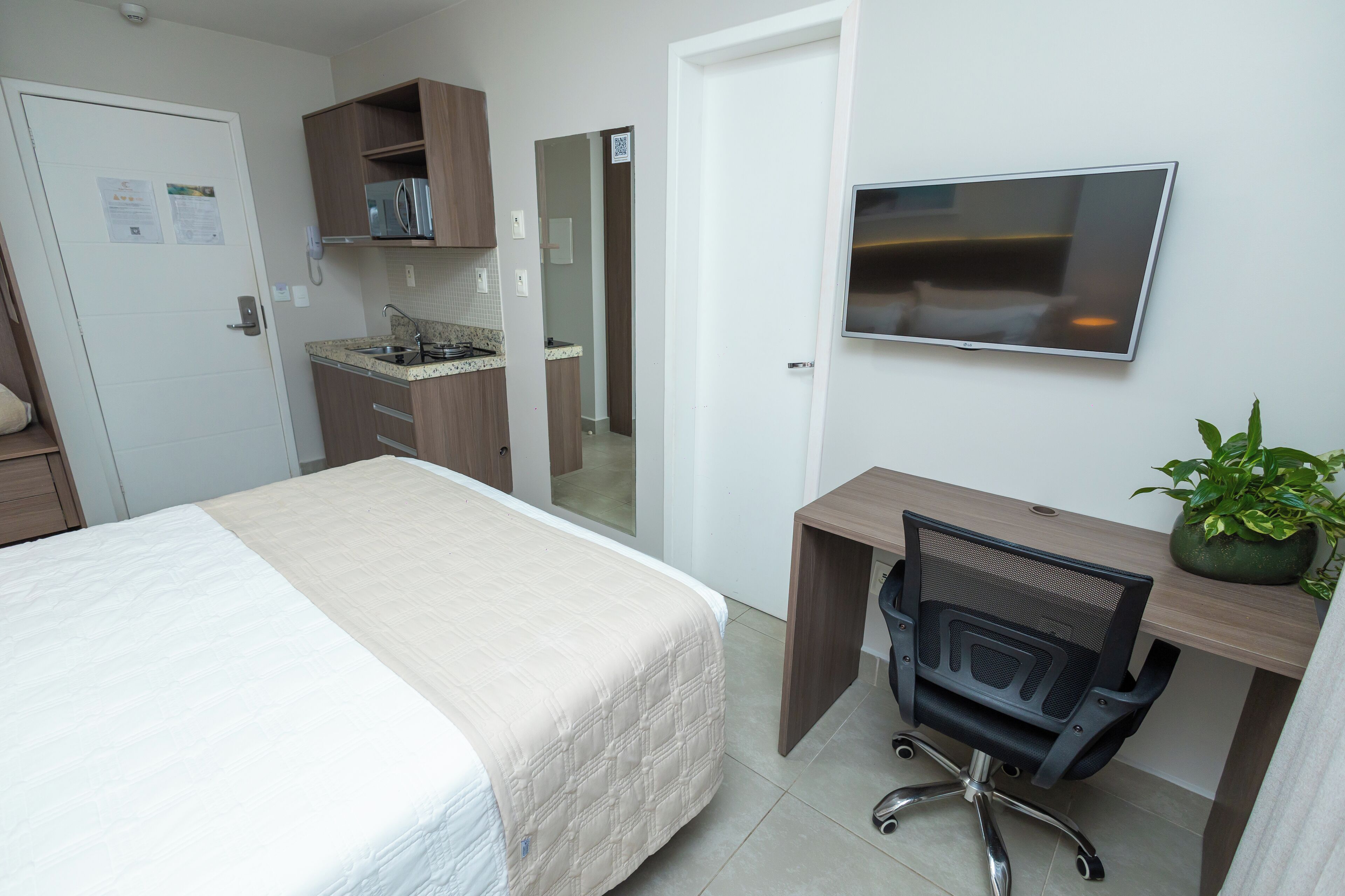 Une chambre d’hôtel comprenant un lit, un bureau avec une chaise, une télévision, un four à micro-ondes et une plante en pot.