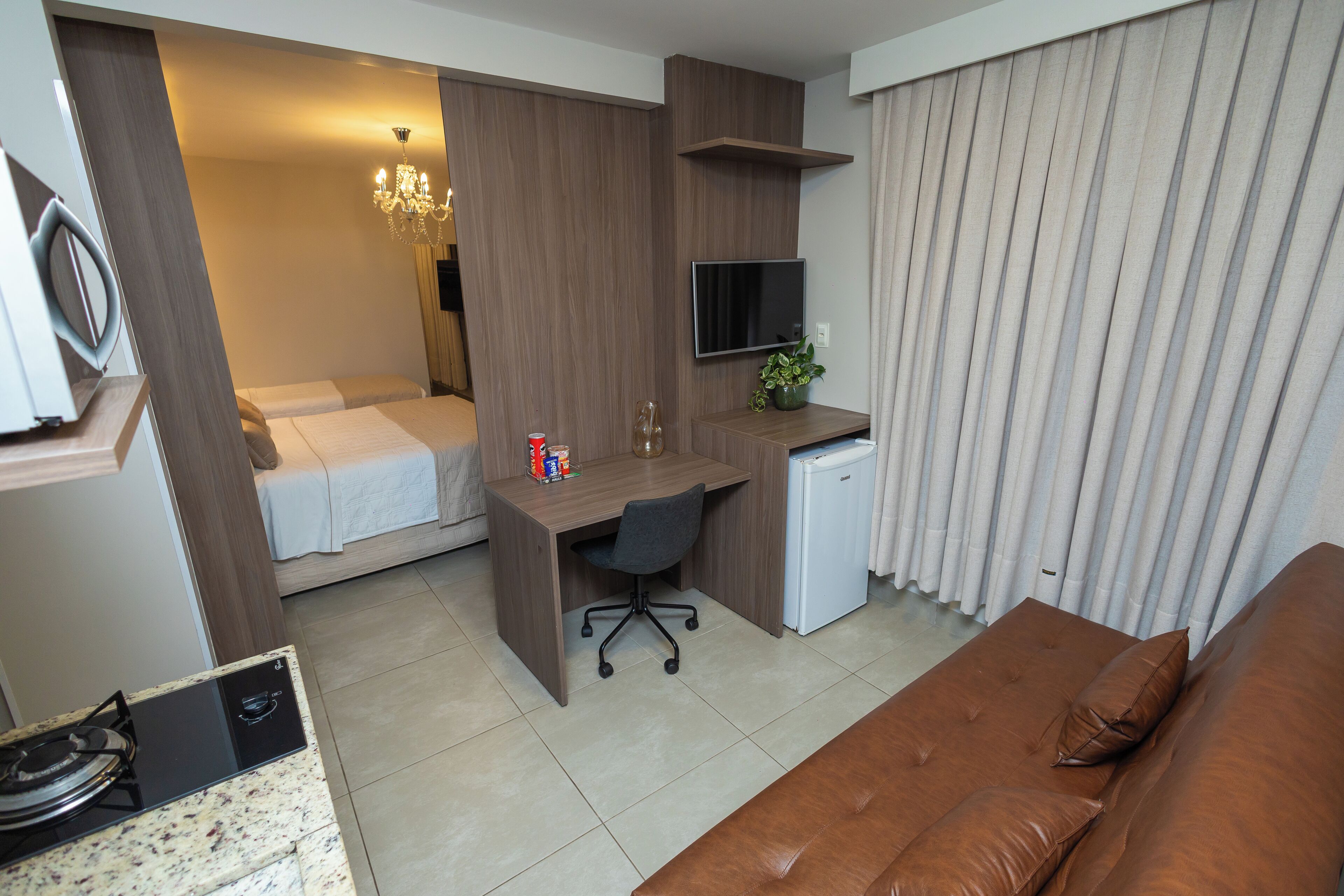 A compact hotel room with a bed, a desk, a chair, a television, and a sofa.