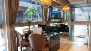 A hotel reception desk with a computer monitor, a plant, and a seating area with chairs.