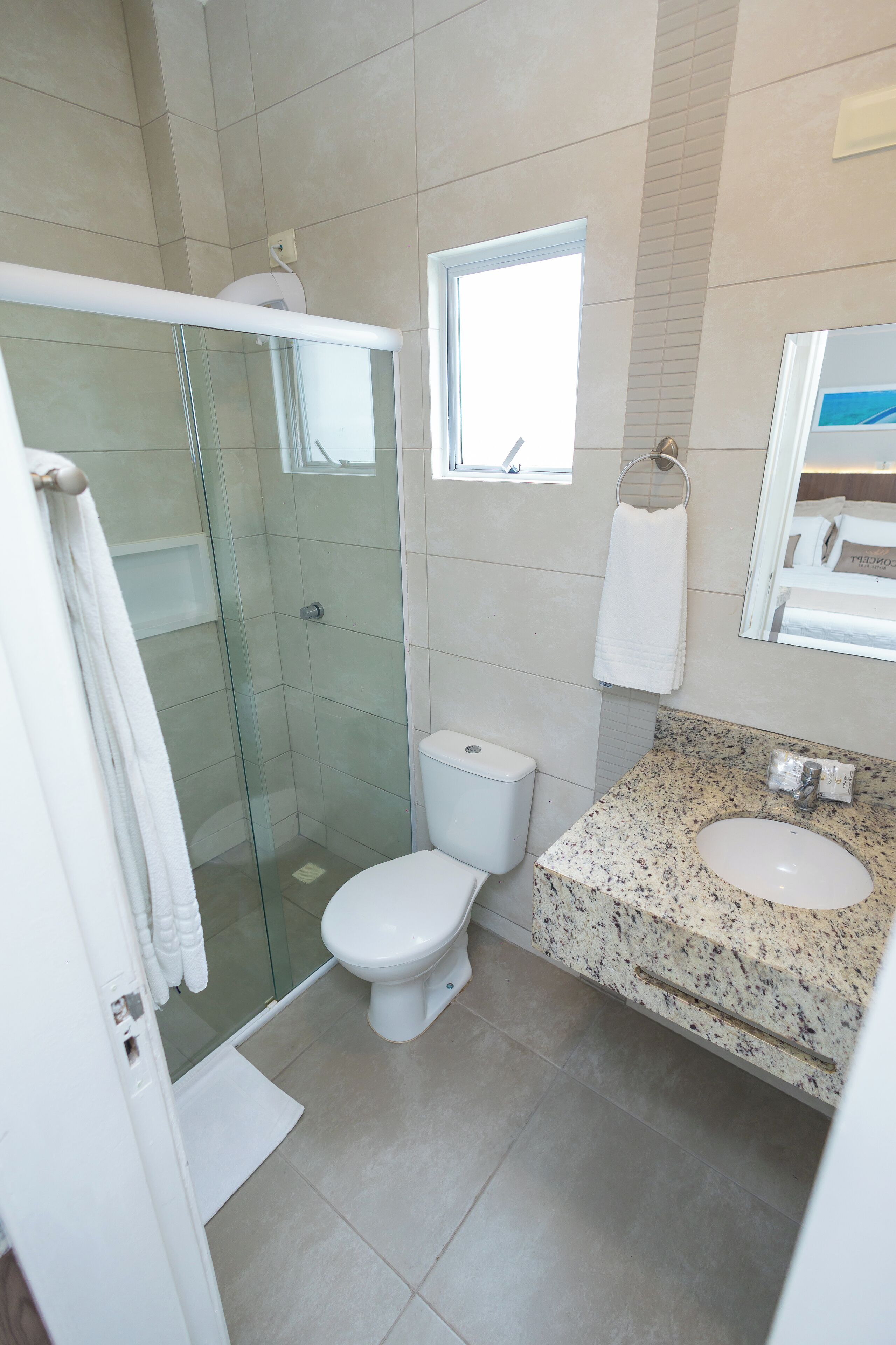 A modern bathroom with a glass-enclosed shower, a toilet, a sink with a granite countertop, and a window providing natural light.