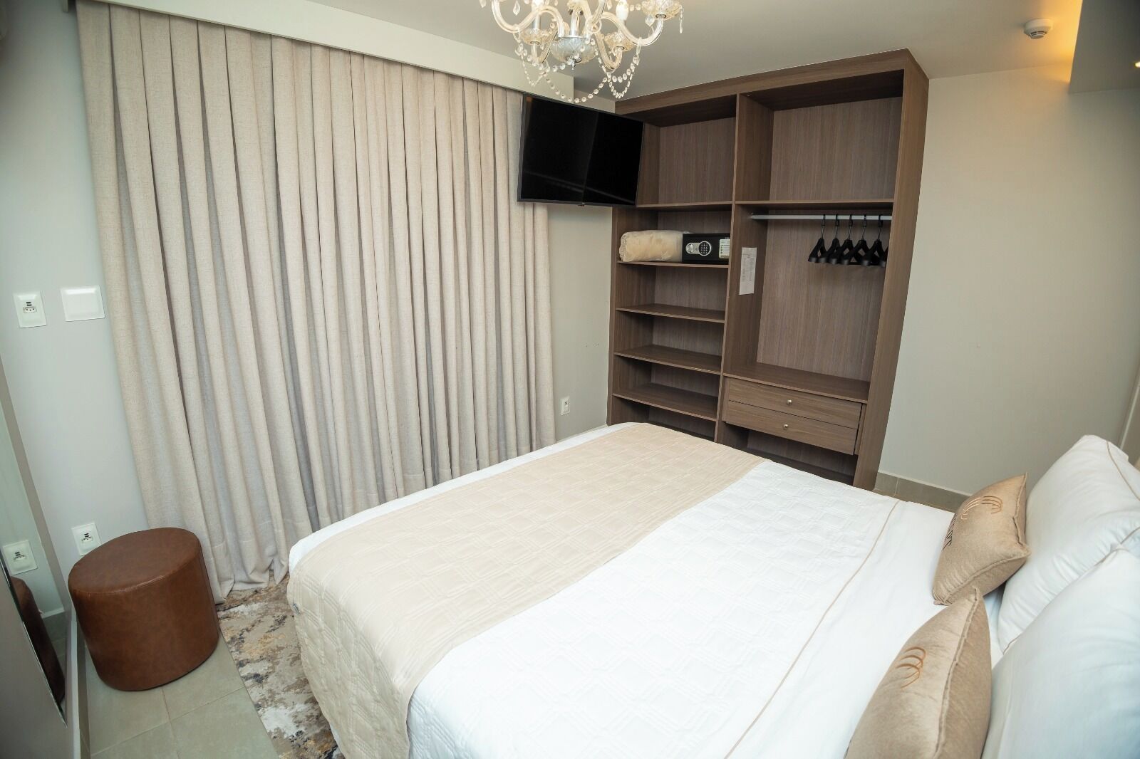 A bedroom with a bed, a wardrobe, a TV, and a small stool.