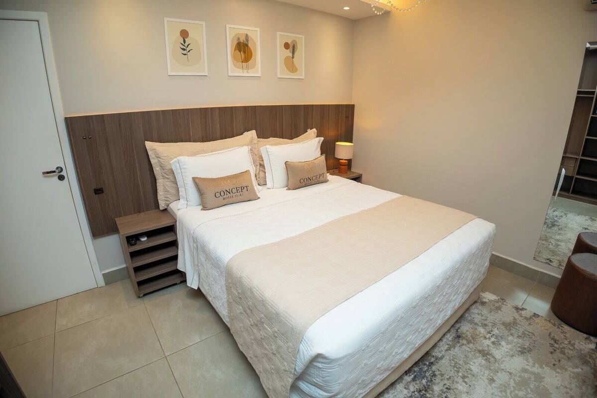 A neatly arranged bedroom with a large bed, a wooden headboard, a bedside table with a lamp, and a small seating area.