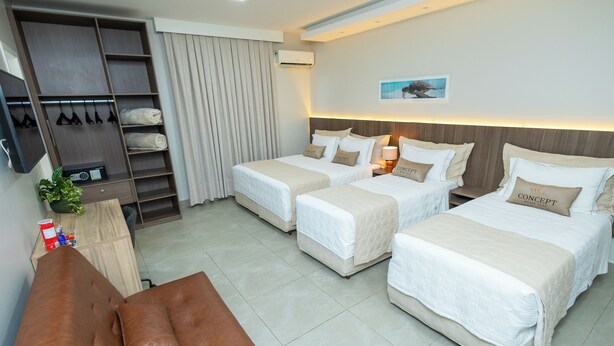 A hotel room with two beds, a brown sofa, a wardrobe, and a desk with a plant.