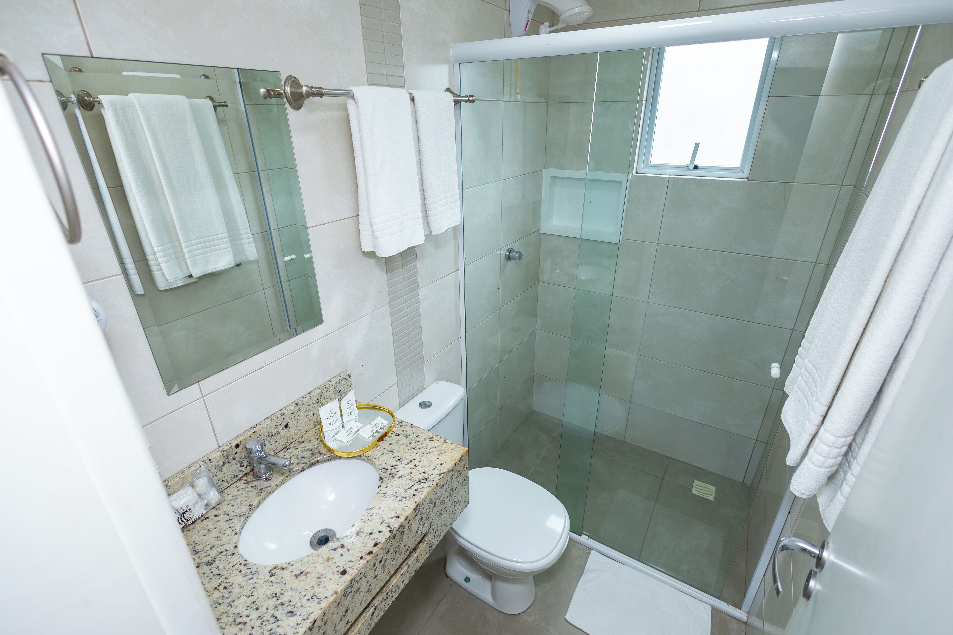 Un baño moderno con cabina de ducha de vidrio, encimera de granito, lavabo blanco y un inodoro.