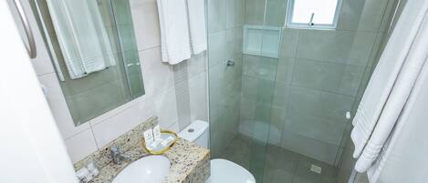 Un baño moderno con cabina de ducha de vidrio, encimera de granito, lavabo blanco y un inodoro.