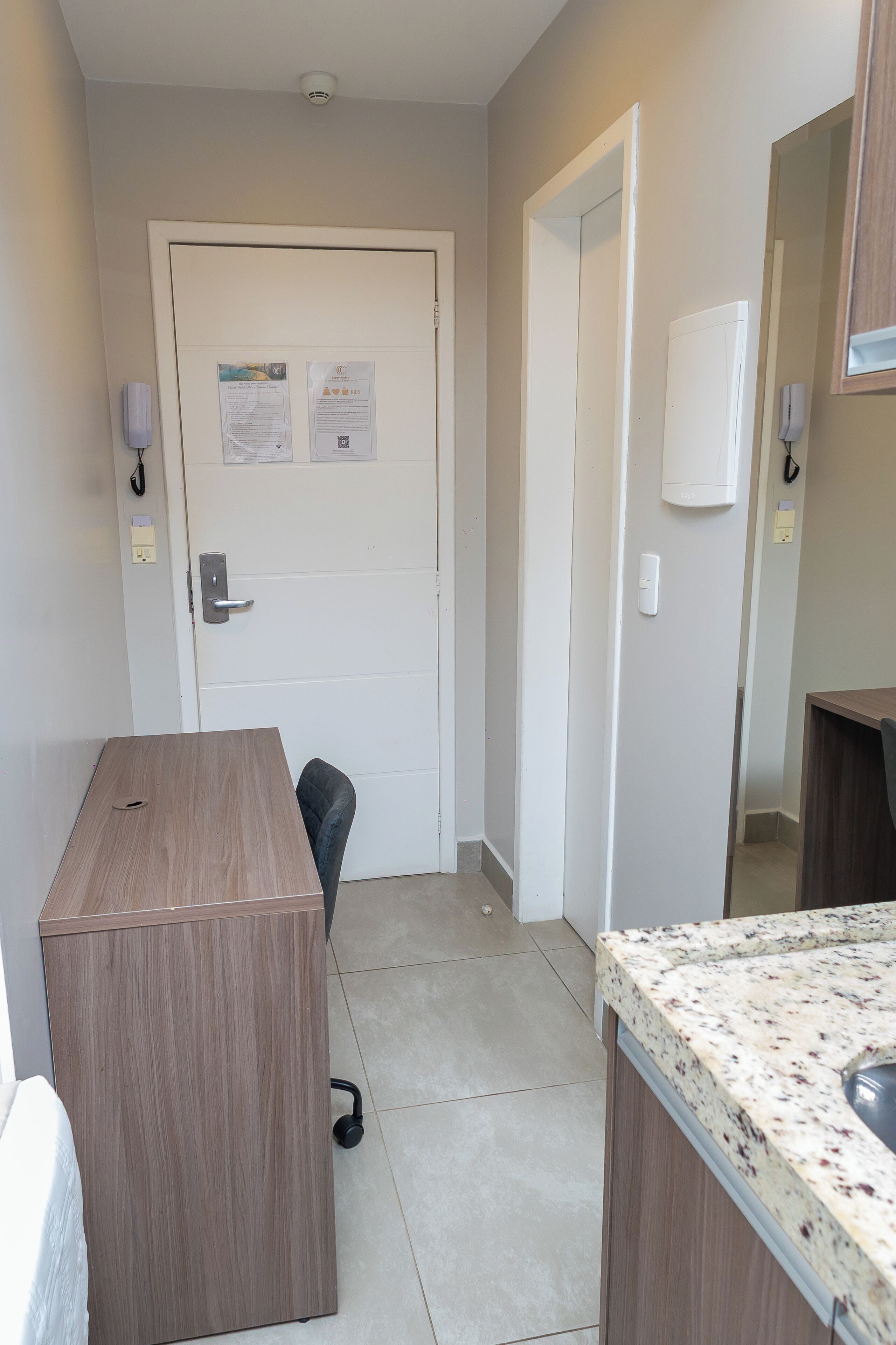 Un baño pequeño y limpio con un escritorio de madera, una silla, un lavamanos y una puerta con un aviso.