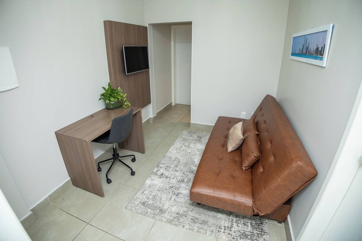 A modern room with a wooden desk, a brown leather sofa, a small potted plant, and a framed picture on the wall.