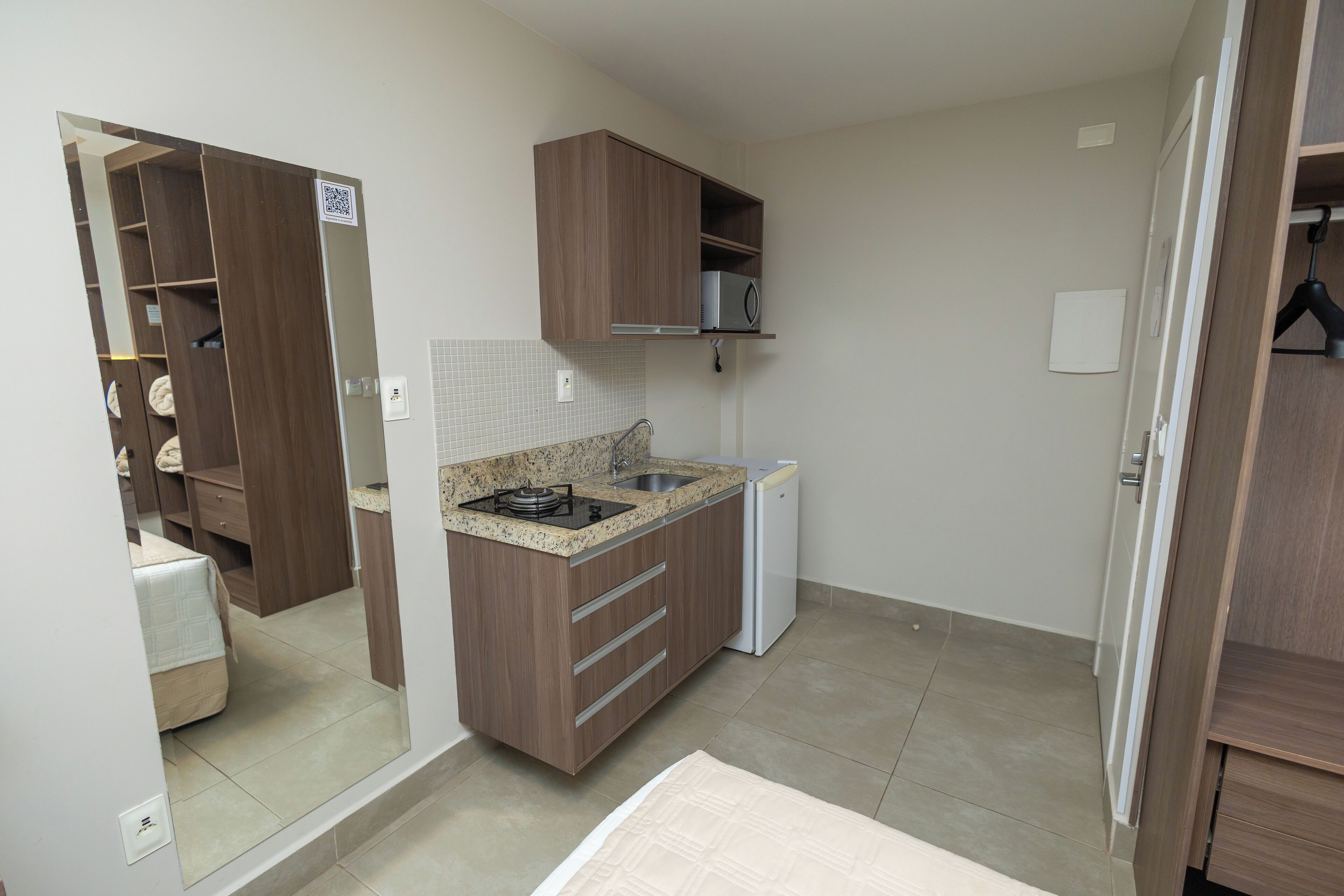 A compact kitchen with a built-in stove, a microwave, and a small refrigerator. There is a wooden cabinet above the stove and a countertop with a sink.