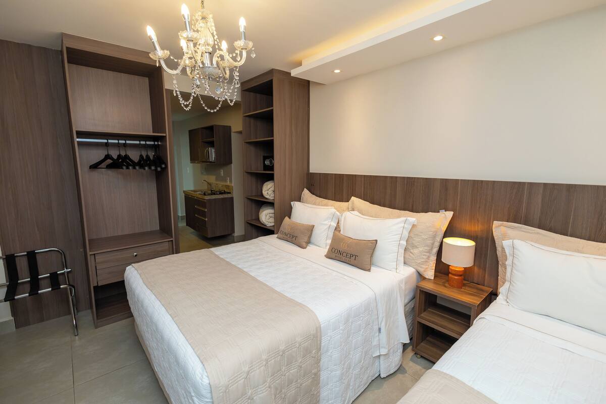 A modern hotel room with a large bed, a wardrobe, a vanity, and a chandelier.