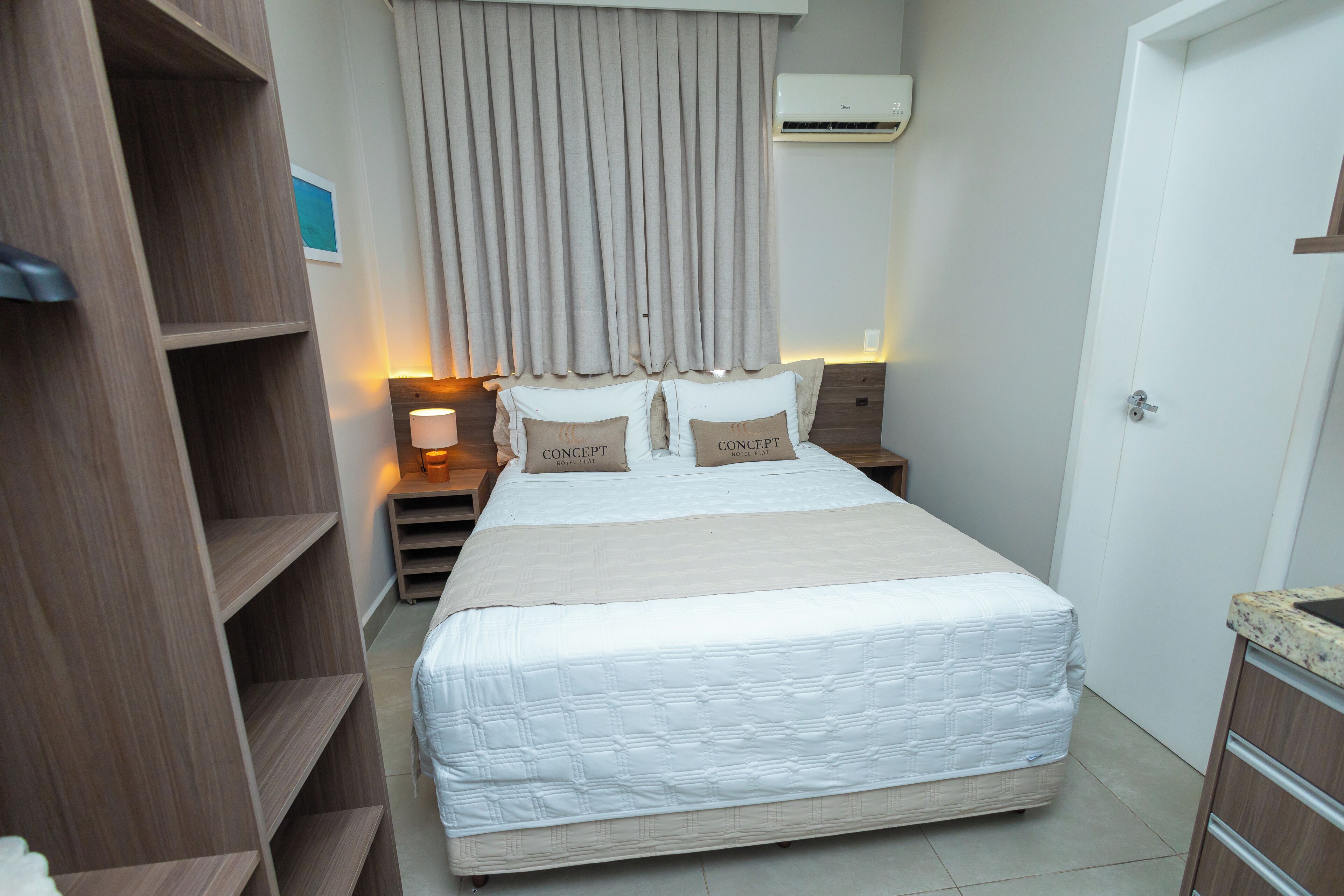 A neatly arranged bedroom with a large bed, a wardrobe, a nightstand, and a wall-mounted air conditioner.
