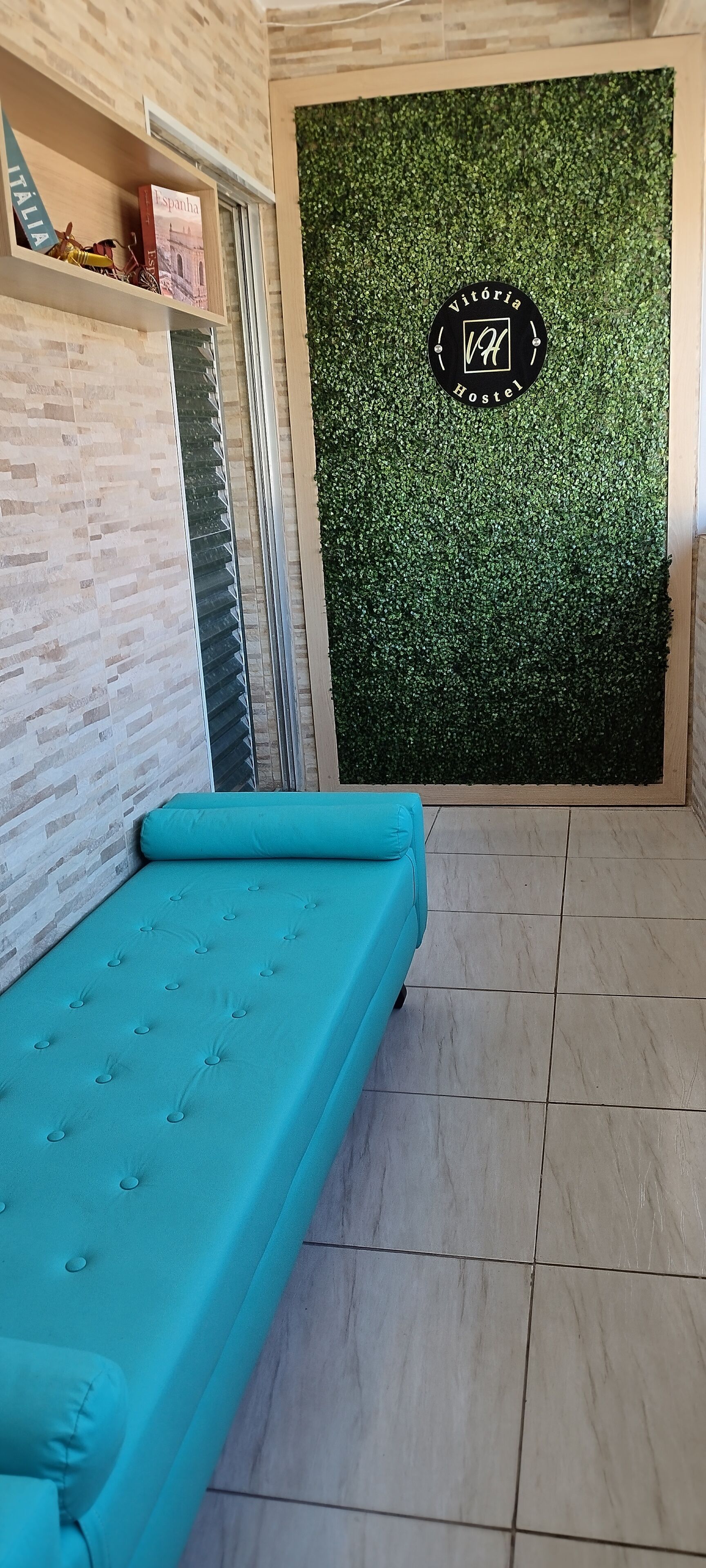 Ein Zimmer mit einem türkisfarbenen Sofa, einer grünen Wand mit einem Logo und einem Fenster mit Jalousien.