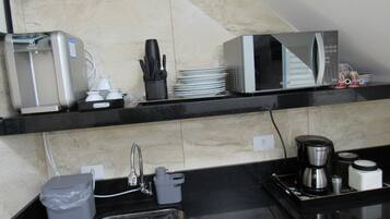 Cozinha equipada com micro-ondas, torradeira e máquina de café. Há uma pia com torneira e um cesto de lixo.