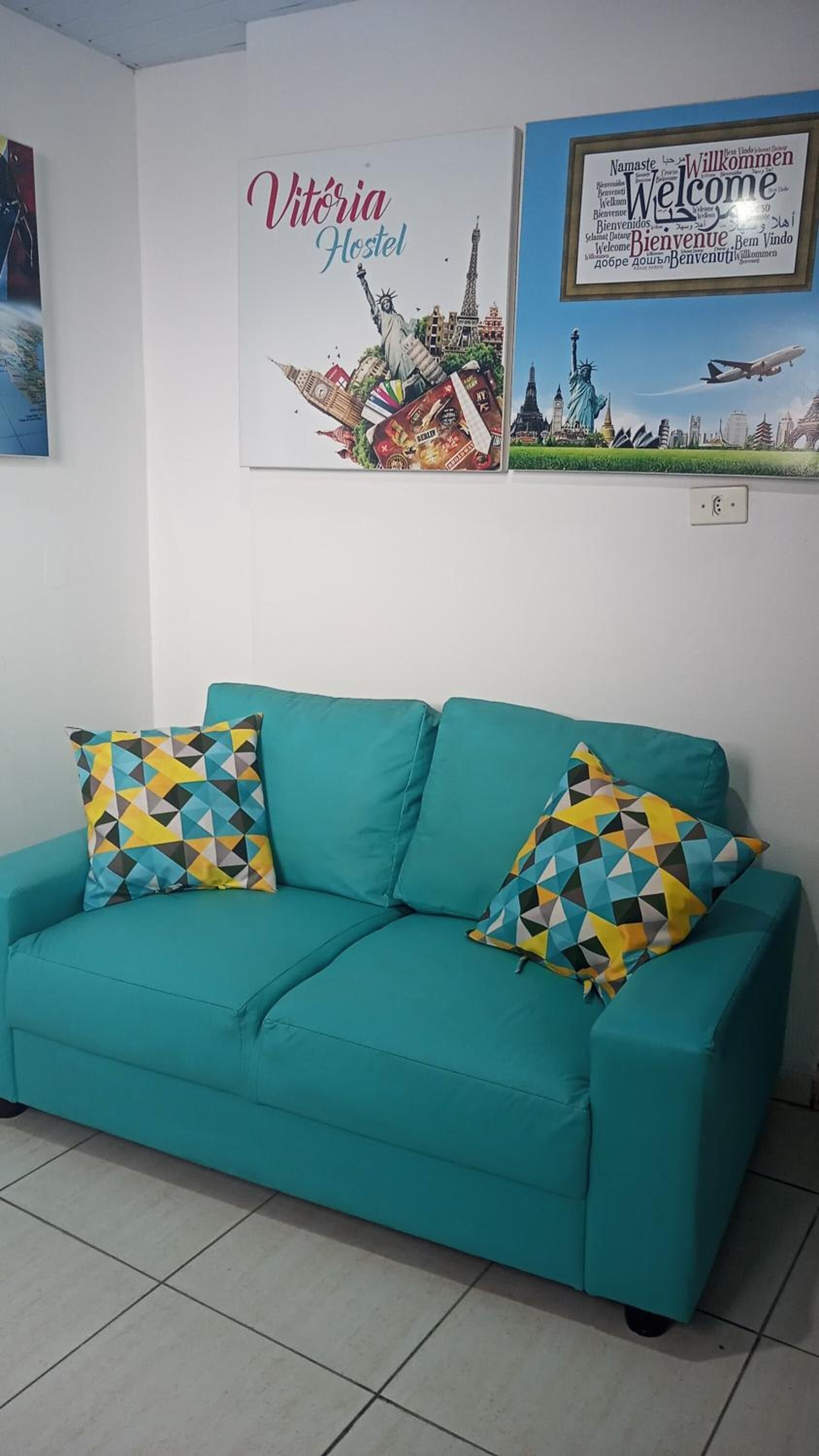 A teal sofa with patterned cushions in a room with a white wall.