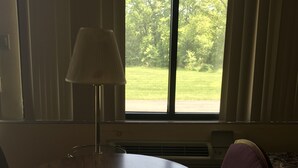 A room with a round table, a chair, a lamp, and a window with a view of trees. - Allenwood Motel (Allentown)