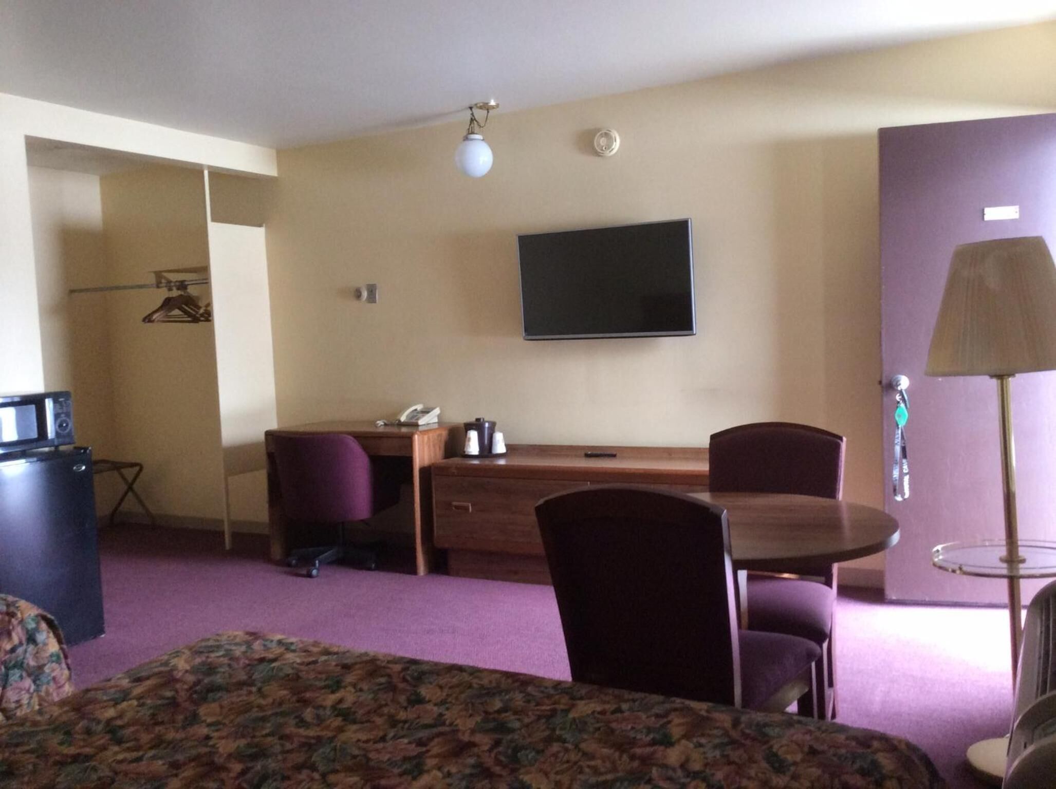 A hotel room with a bed, a desk, a chair, a television, and a lamp.