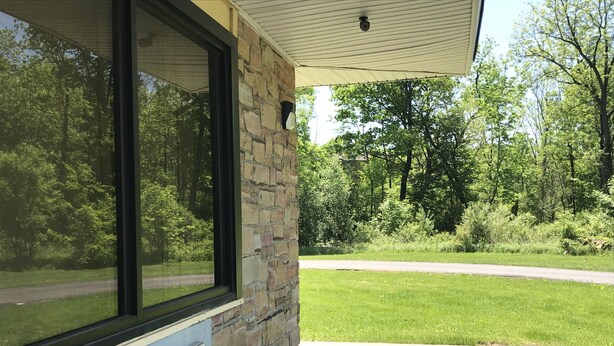 A covered porch with a stone wall and large windows overlooking a grassy area and trees. - Allenwood Motel (Allentown)