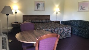 A hotel room with a bed, a sofa, a round table, and two lamps. - Allenwood Motel (Allentown)