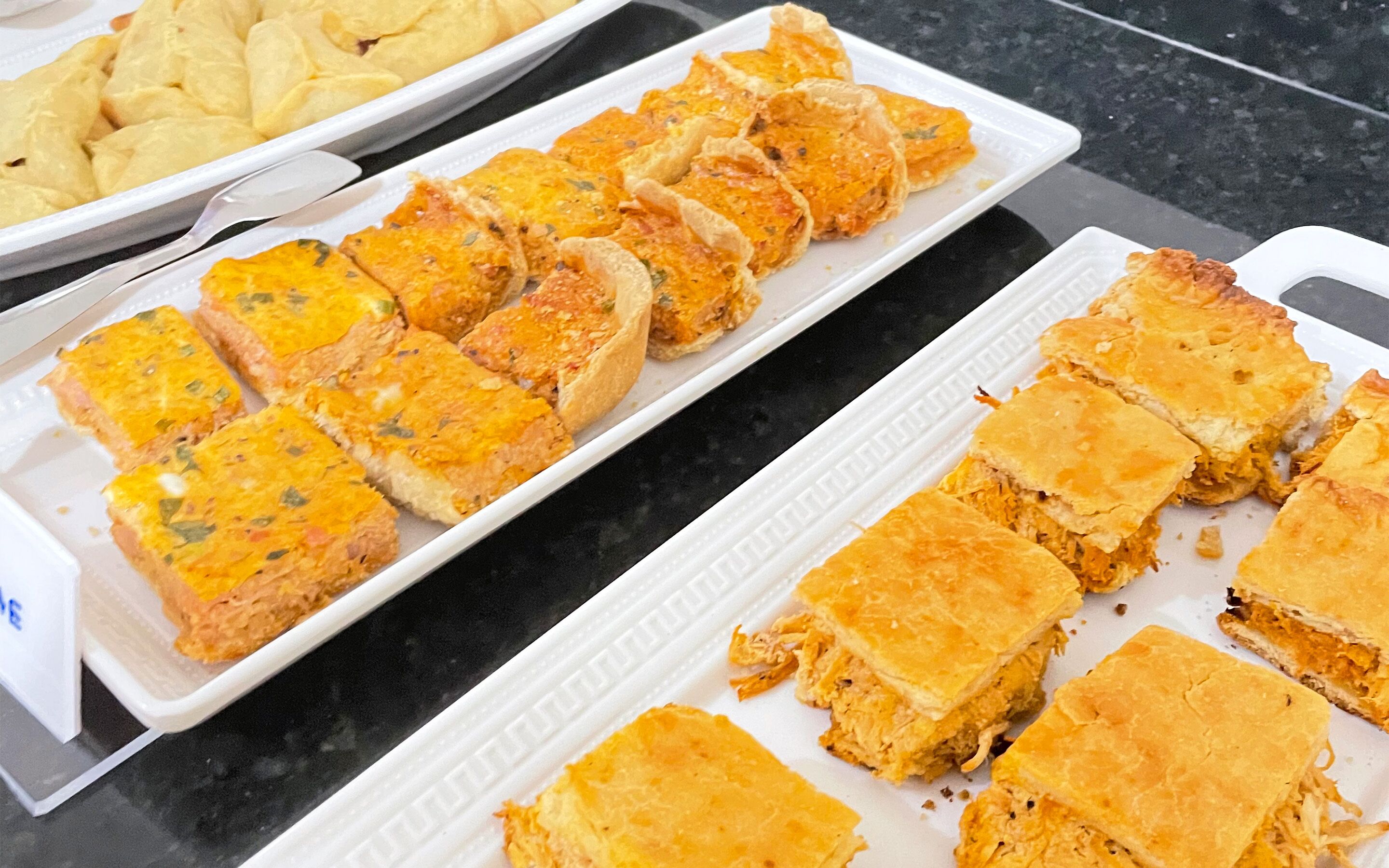 A buffet table with various dishes, including a tray of golden-brown baked items and a plate of golden-brown fried items.