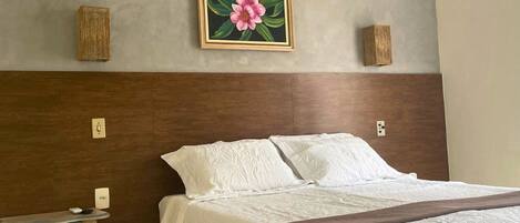 Habitación de hotel con una cama, una mesita de noche, un cuadro de una flor y un cabecero de madera.