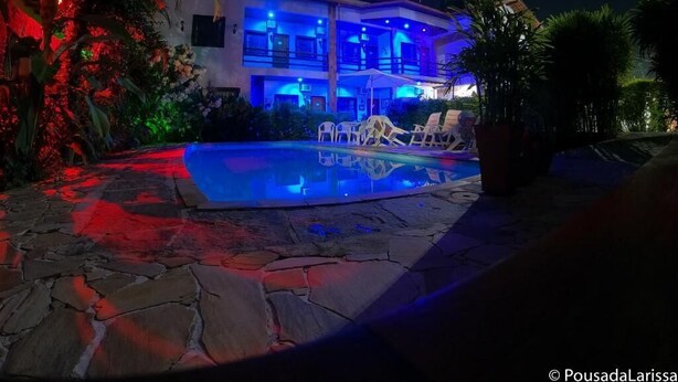 A modern hotel with a swimming pool, lounge chairs, and a well-lit exterior at night. - Pousada Larissa (Paraty)