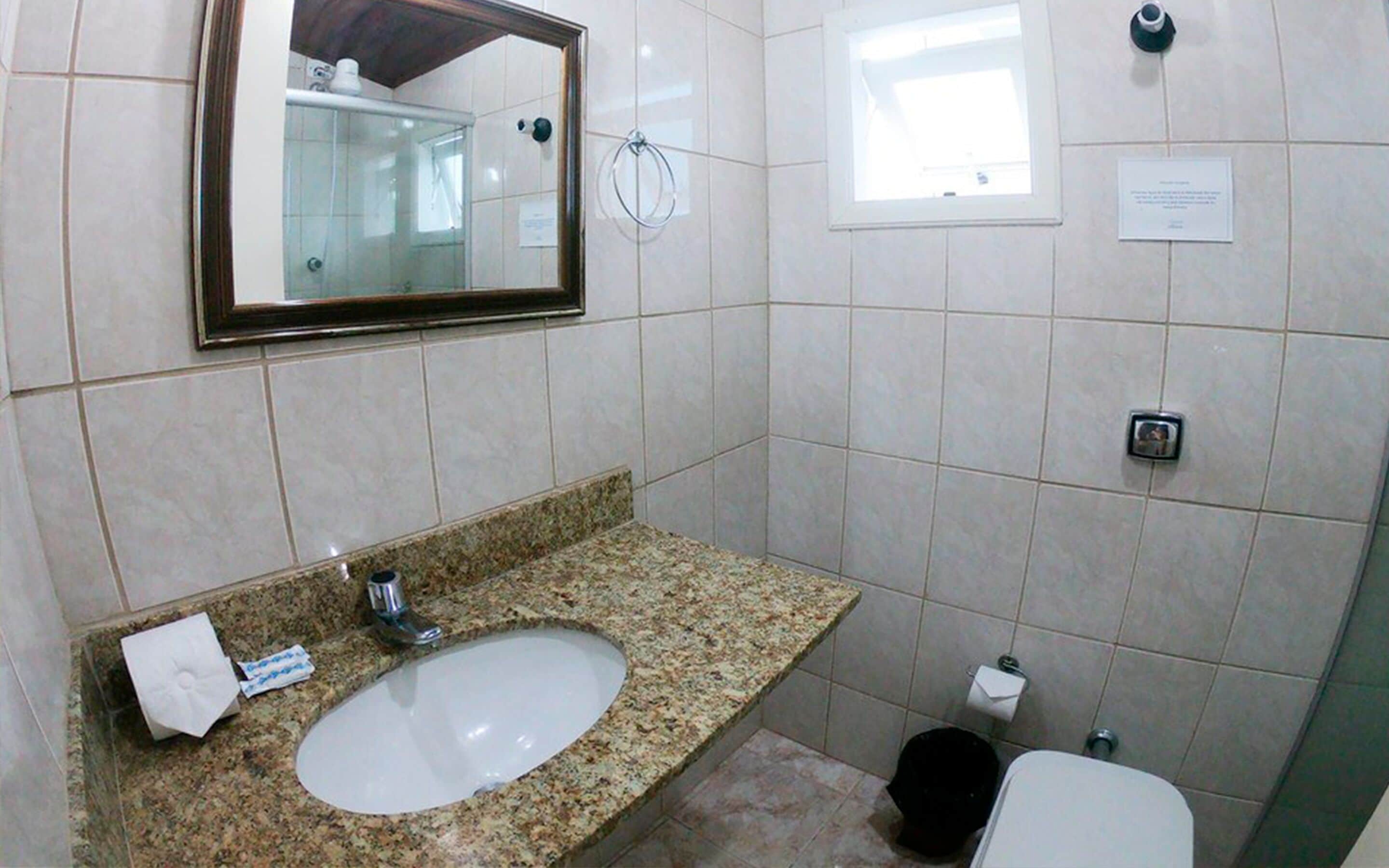 A bathroom with a granite countertop sink, a mirror, a toilet, and a small window.