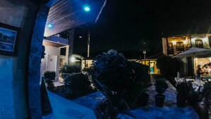 A nighttime view of a building with a covered outdoor area, potted plants, and a staircase leading to an upper level. - Pousada Larissa (Paraty)