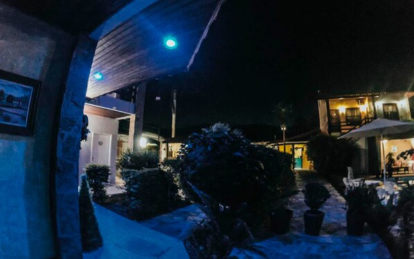 Ein Gebäude bei Nacht mit einem überdachten Außenbereich, Kübelpflanzen und einer Treppe, die zu einer oberen Ebene führt.