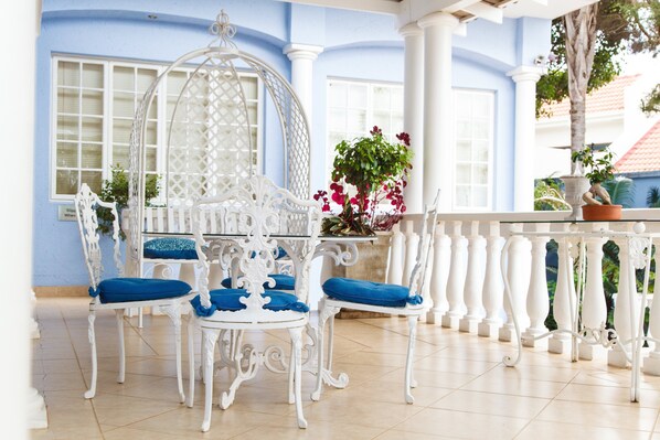 Una mesa blanca ornamentada con cojines azules, rodeada de sillas blancas, en una habitación con paredes azules y columnas blancas.