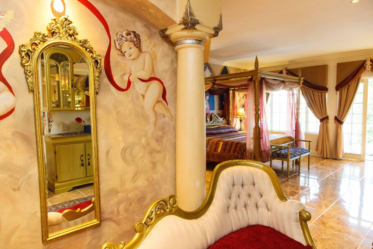 A luxurious bedroom with a large ornate bed, a mirror, and a decorative column.