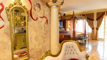 A luxurious bedroom with a large ornate bed, a mirror, and a decorative column.