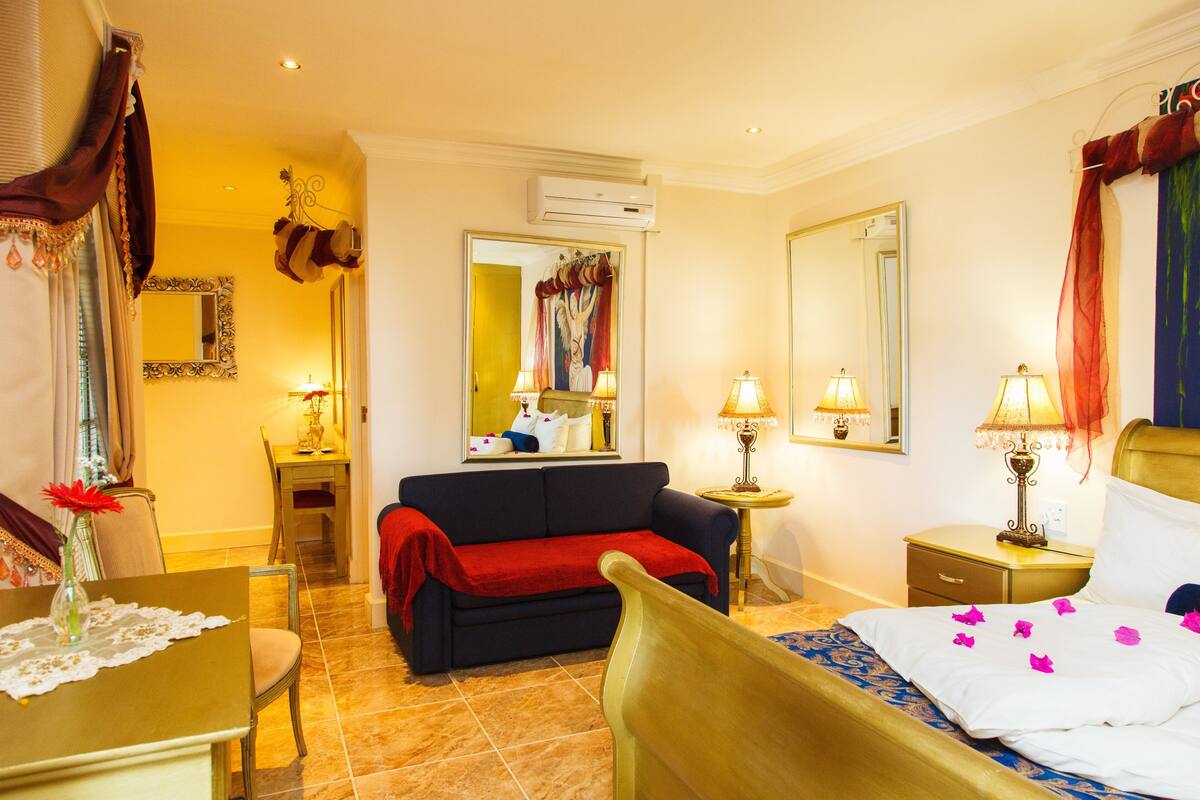 A hotel room with a bed, a sofa, a dining table, and a mirror.