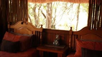 A wooden bench with a small table and a statue in front of a window with a view of trees.