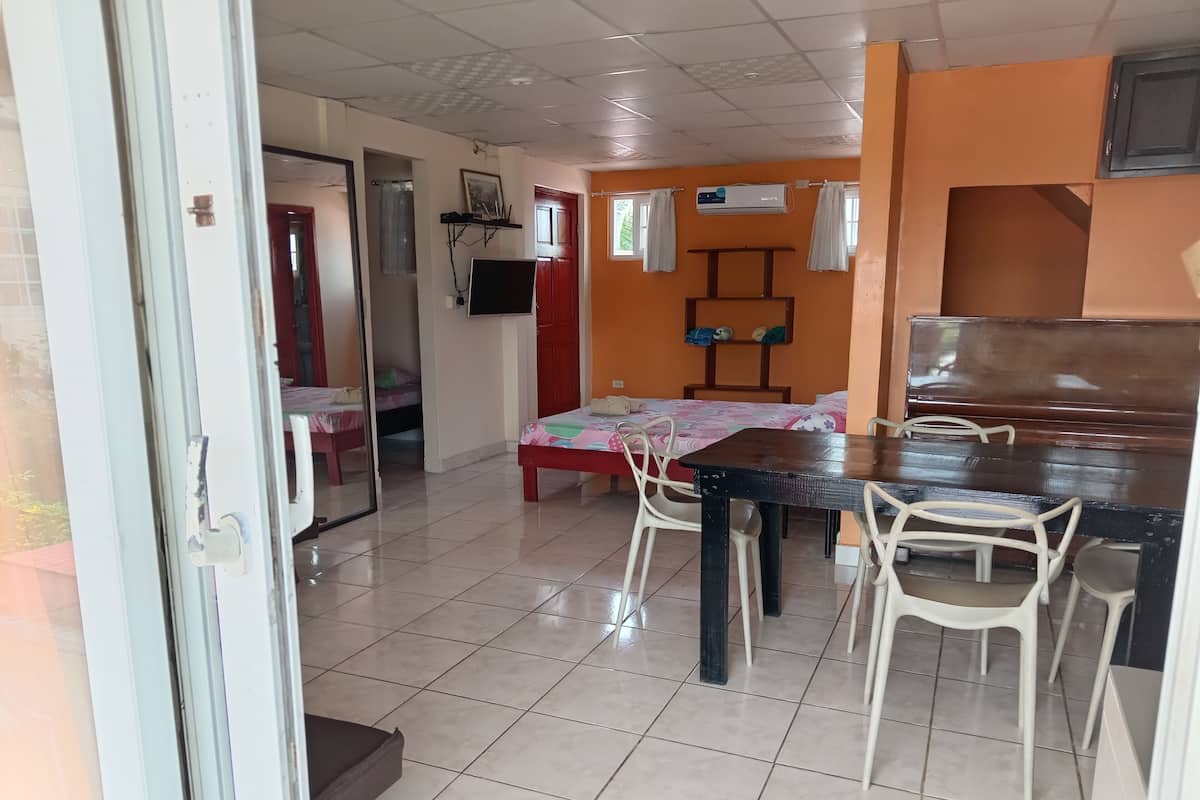 A room with a tiled floor, a bed with a floral bedspread, a table with chairs, and an air conditioning unit on the wall.
