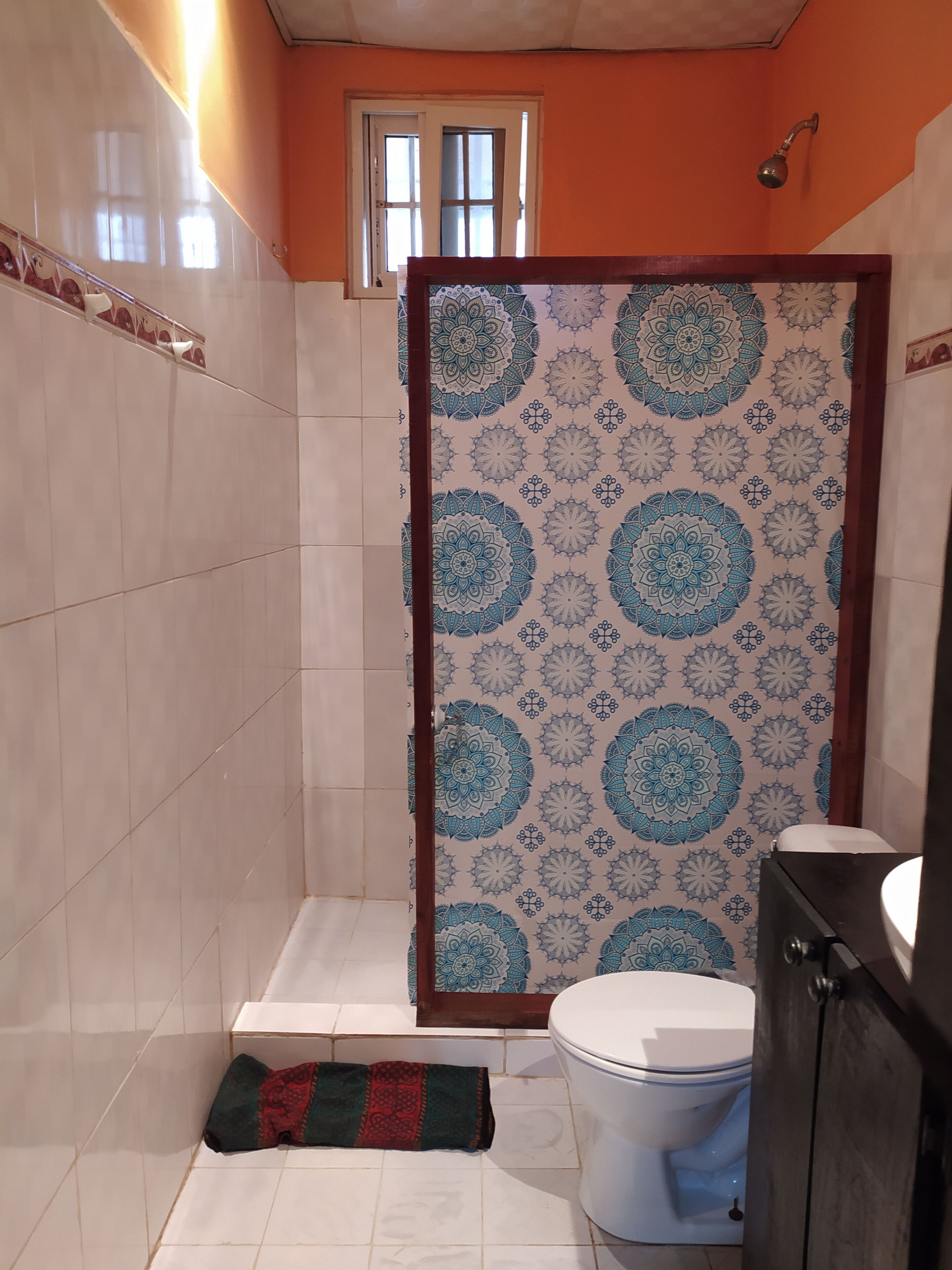 Un baño con cortina de ducha adornada con un diseño de mandala azul y blanco, un inodoro blanco y un armario de madera.