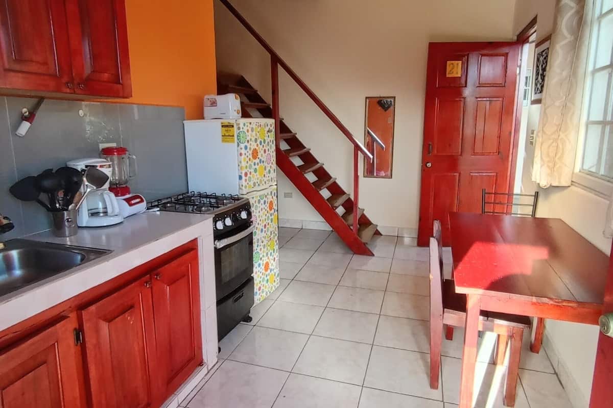 A kitchen with red cabinets, a stove, a refrigerator, and a dining table.