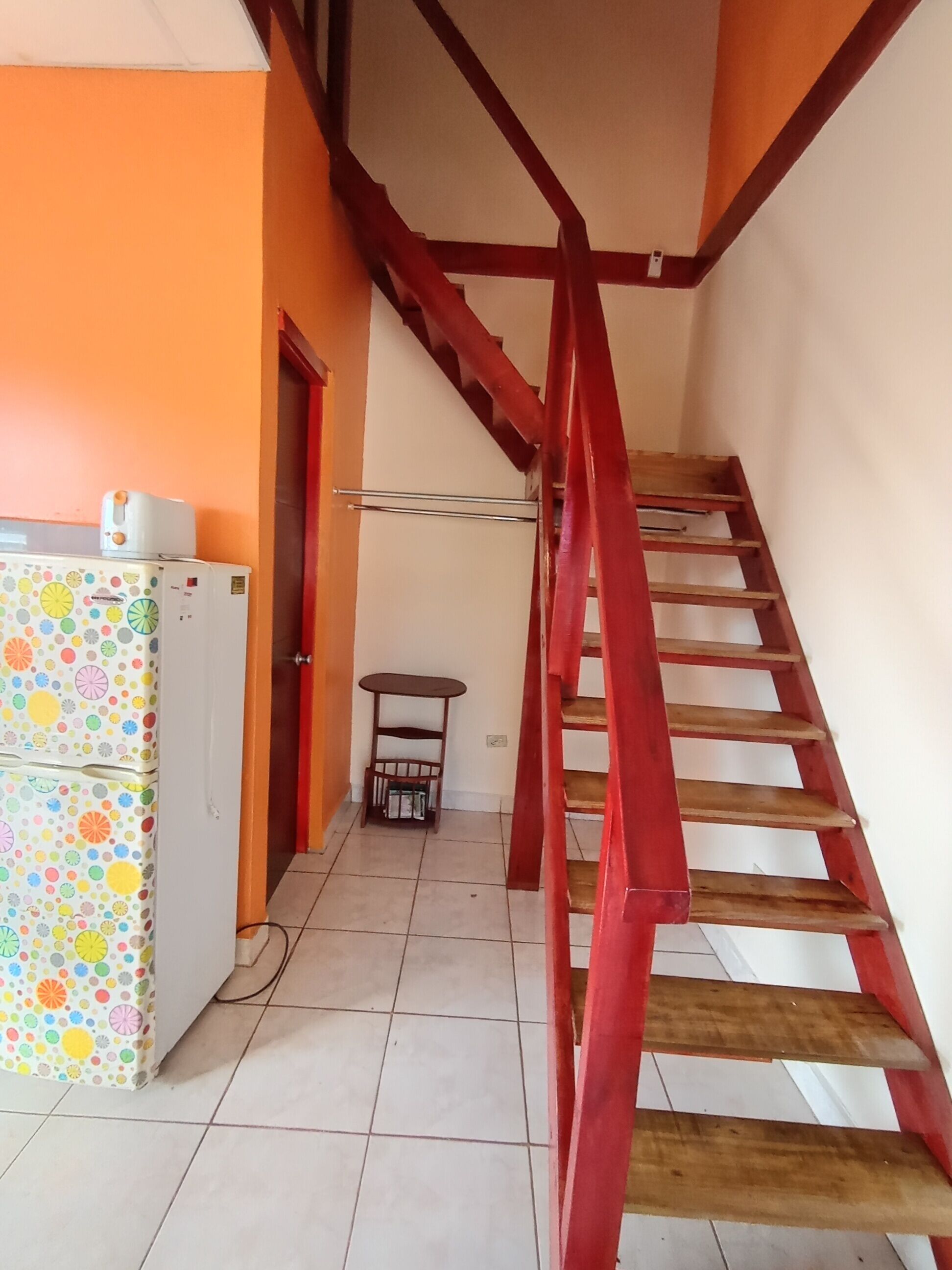 Una escala amb barana vermella que condueix a un aterratge. Es veu una nevera amb un dibuix colorit a l'esquerra.