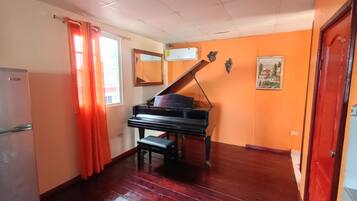 A room with a piano, a refrigerator, and a painting on the wall.