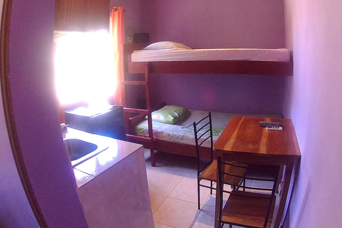 A bunk bed with a desk and chair, a window with curtains, and a small kitchenette area.