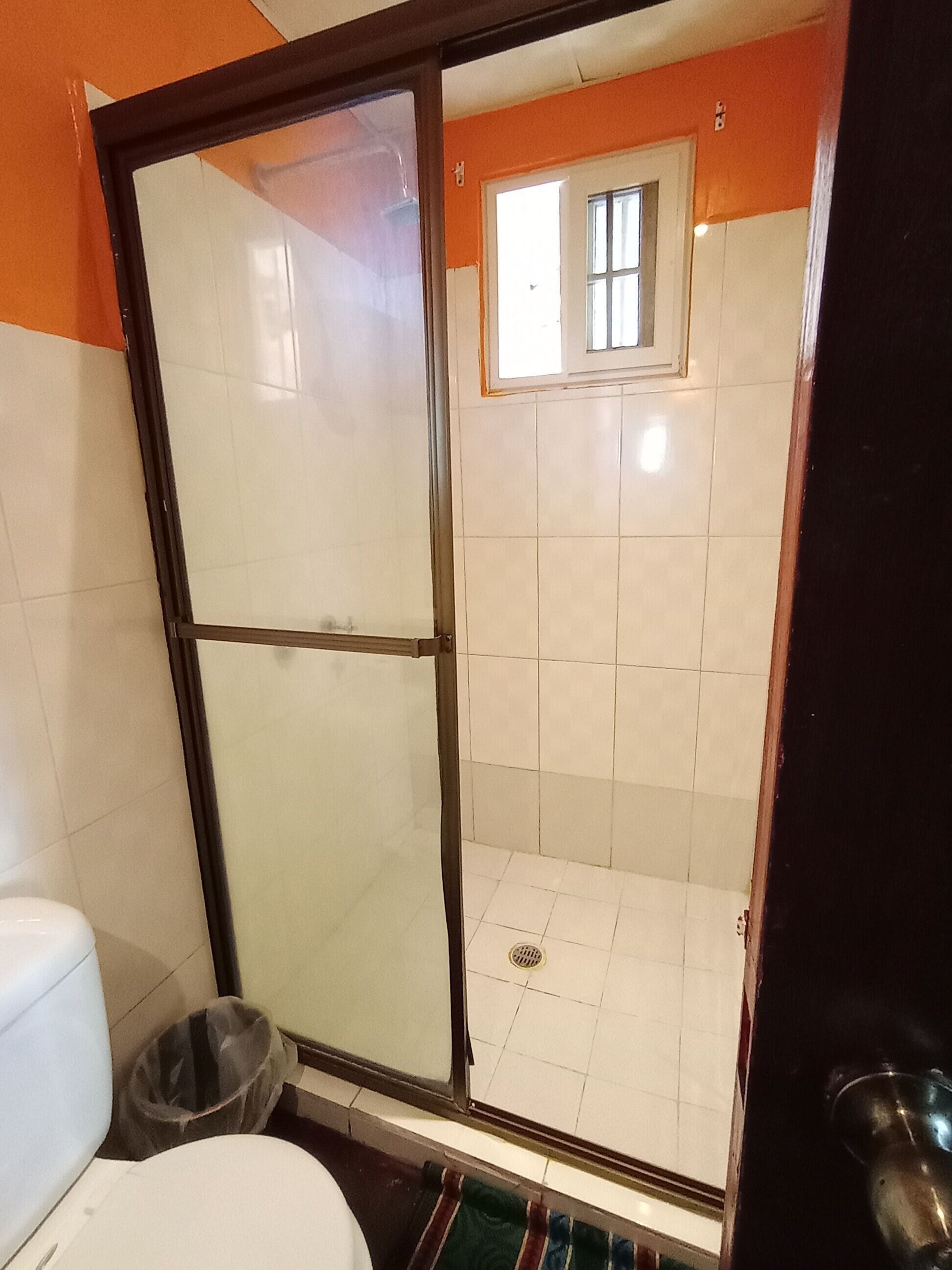 A bathroom with a glass shower enclosure, a toilet, and a trash bin.