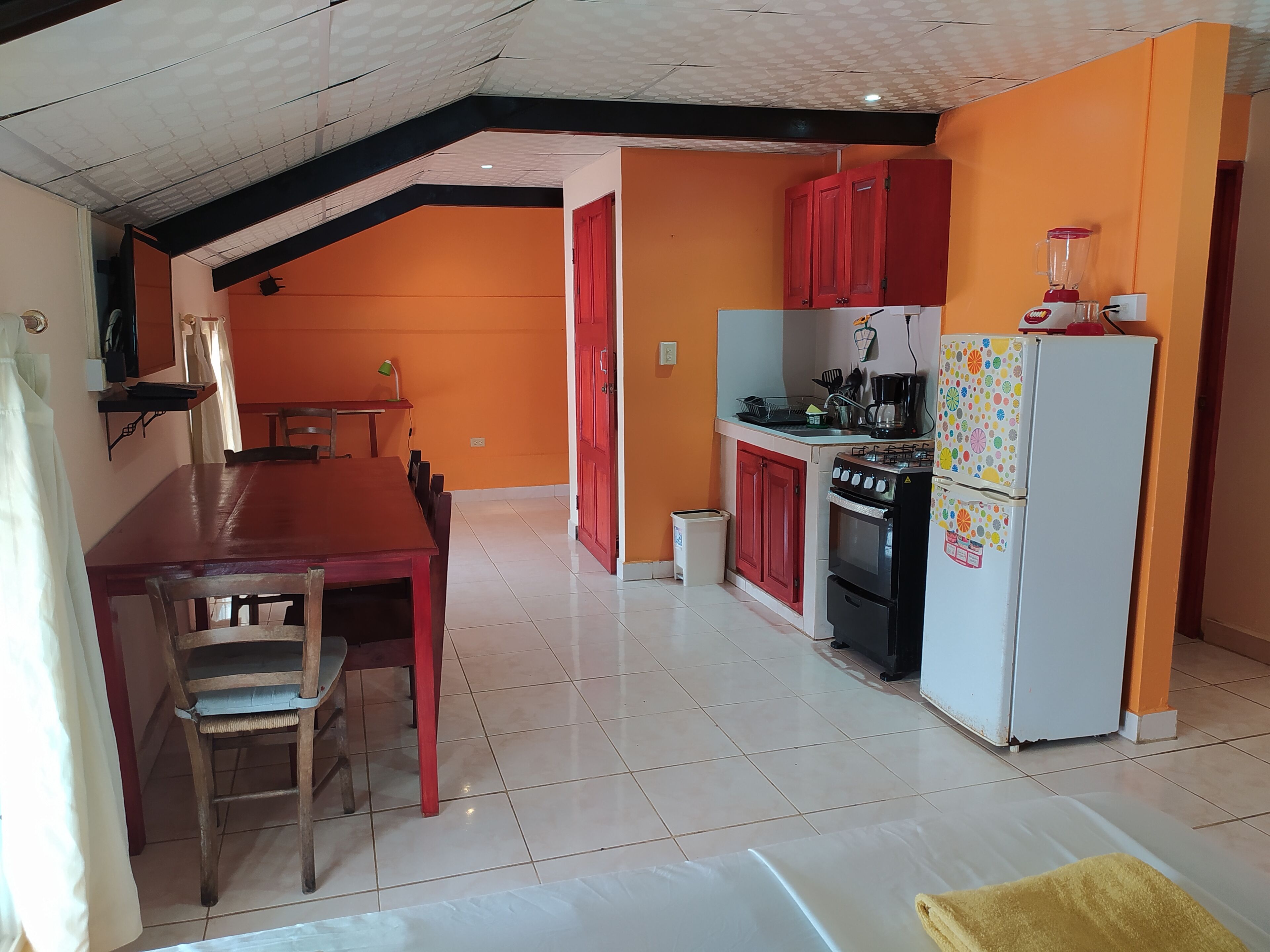 A compact kitchen with a dining area, featuring a red table, chairs, and a small dining table with a lamp.