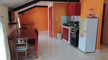 A compact kitchen with a dining area, featuring a red table, chairs, and a small dining table with a lamp.