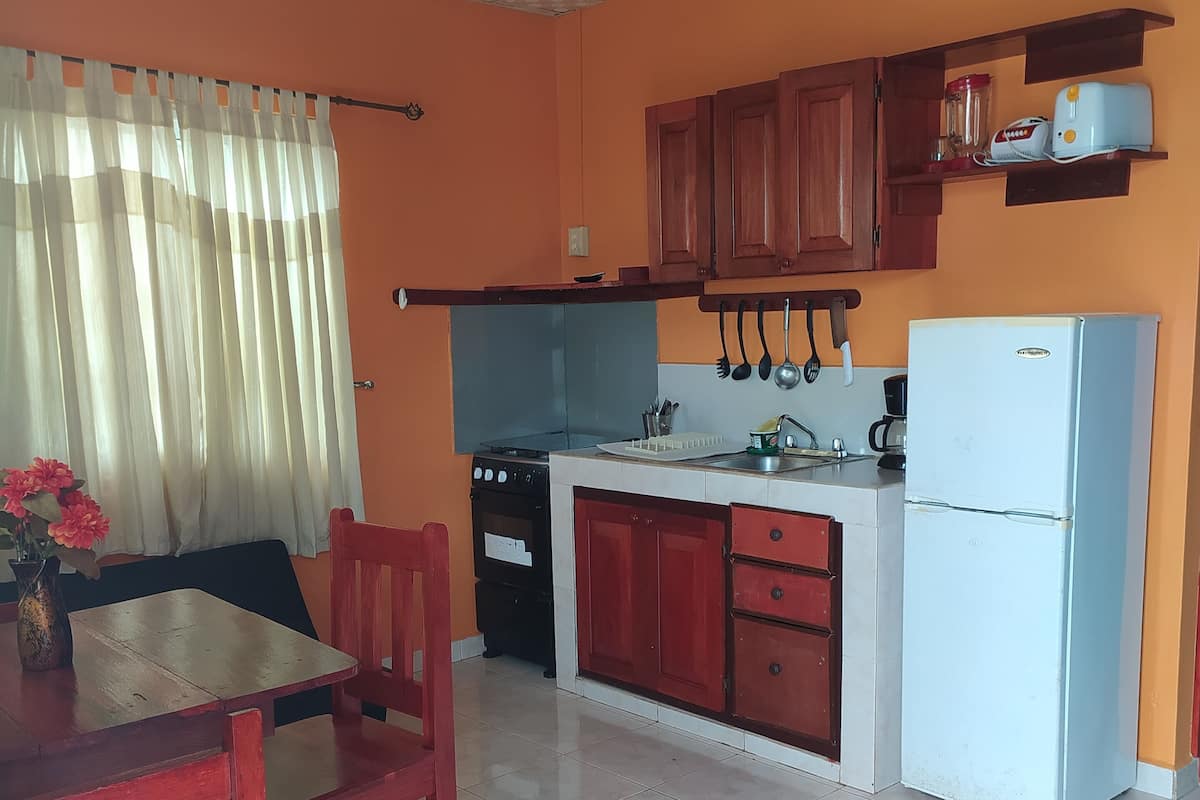A compact kitchen with a dining area, featuring a stove, sink, and refrigerator.