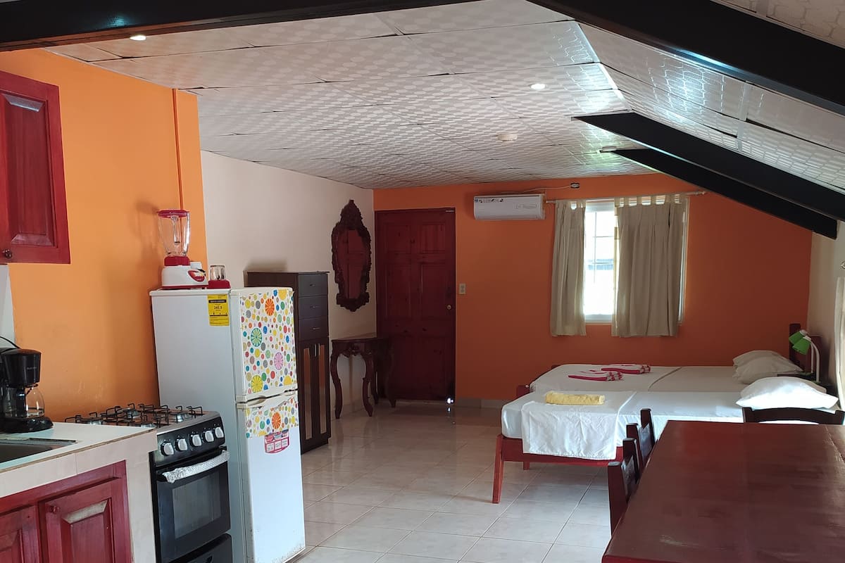 A compact kitchen with a stove, oven, and refrigerator, leading to a bedroom with a bed and a window.