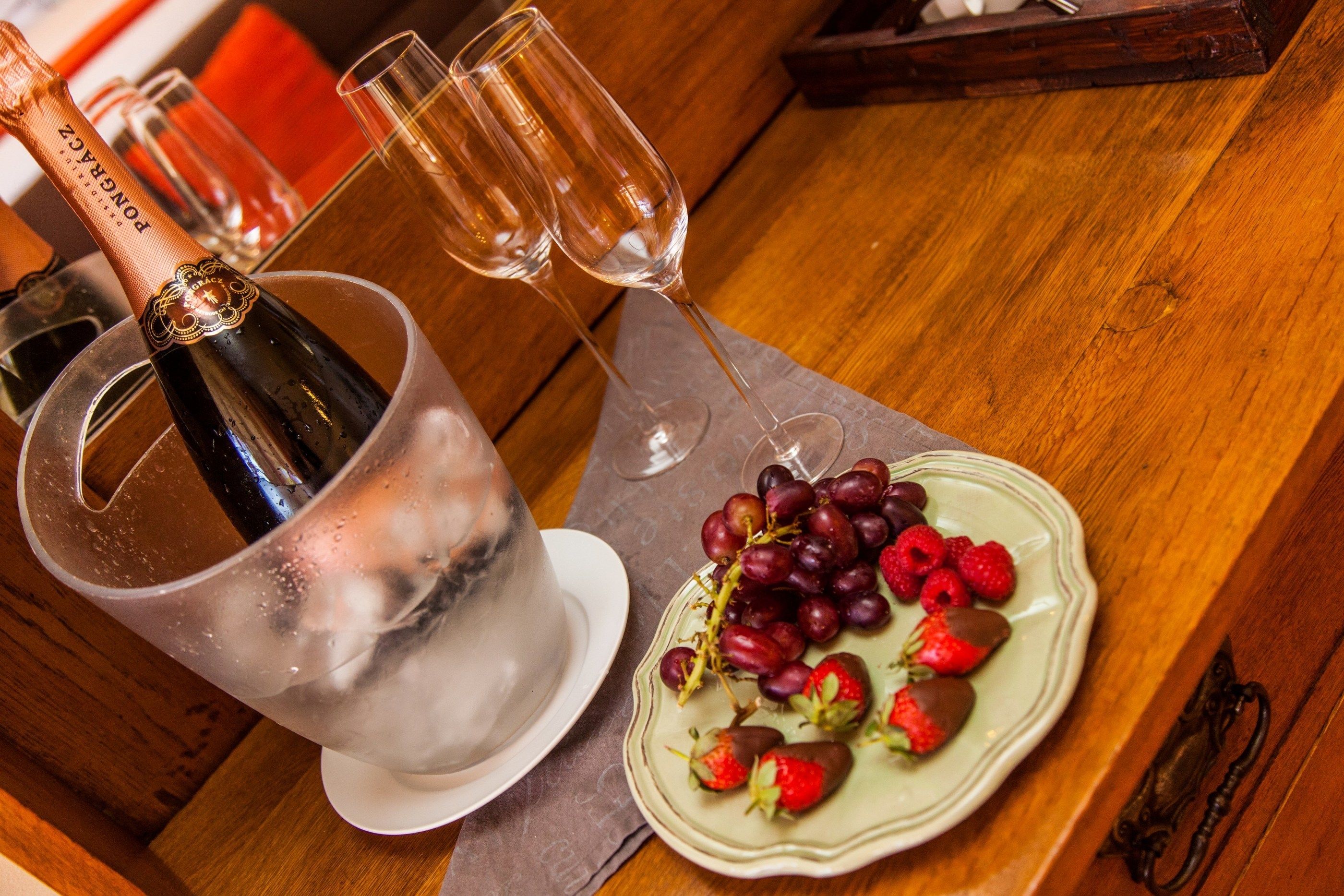 Eine Champagnerflasche, zwei Gläser und ein Teller mit Trauben und Erdbeeren auf einem Holztisch.