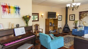 A living room with a piano, a blue sofa, a television, and a fireplace. - 3@Marion Guesthouse (Pretoria)