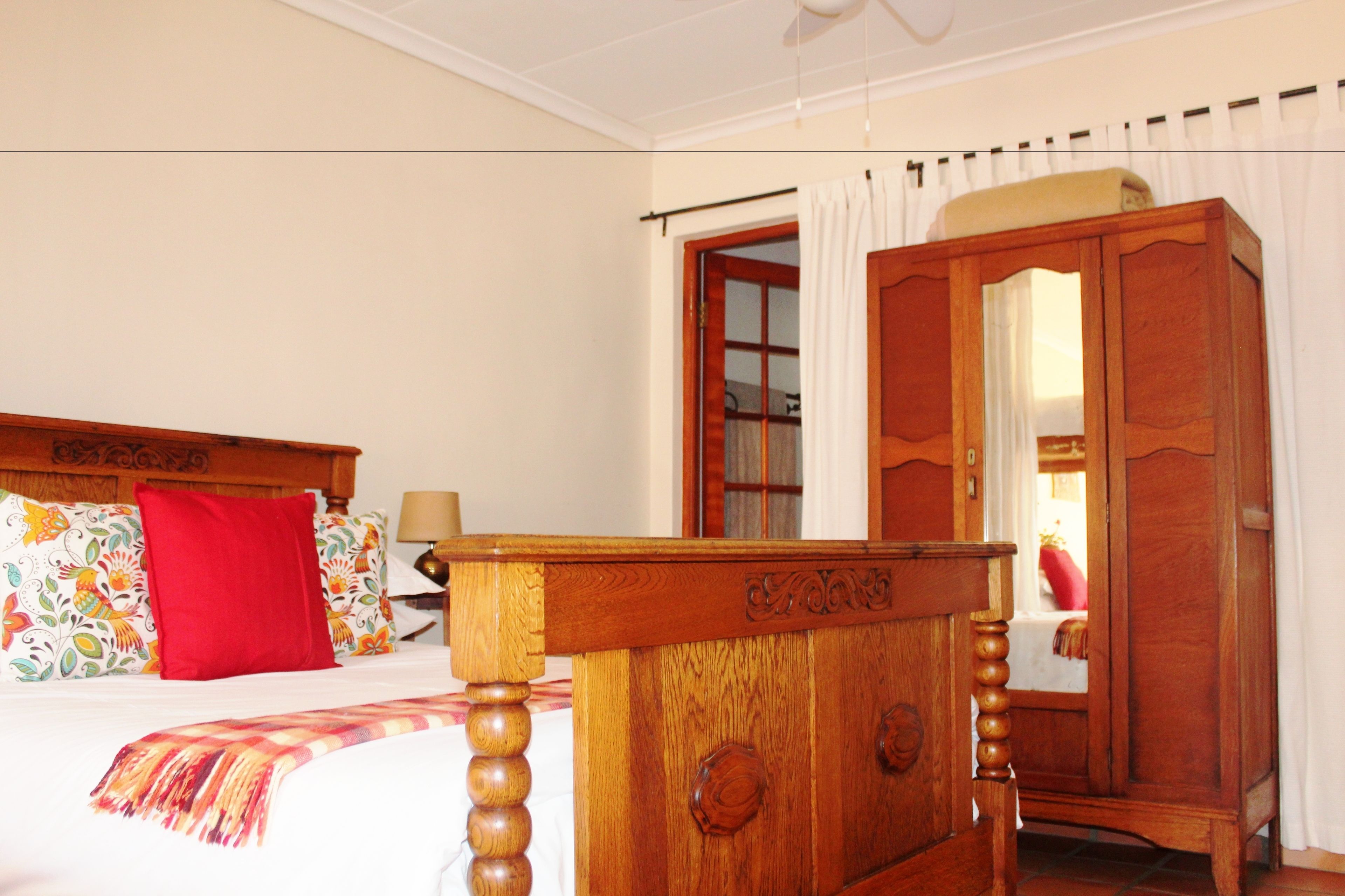 Un dormitorio con estructura de cama de madera, almohada roja, mesita de noche de madera y armario con espejo.