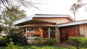A building with a curved roof, a covered porch, and a garden area with various plants. - 3@Marion Guesthouse (Pretoria)