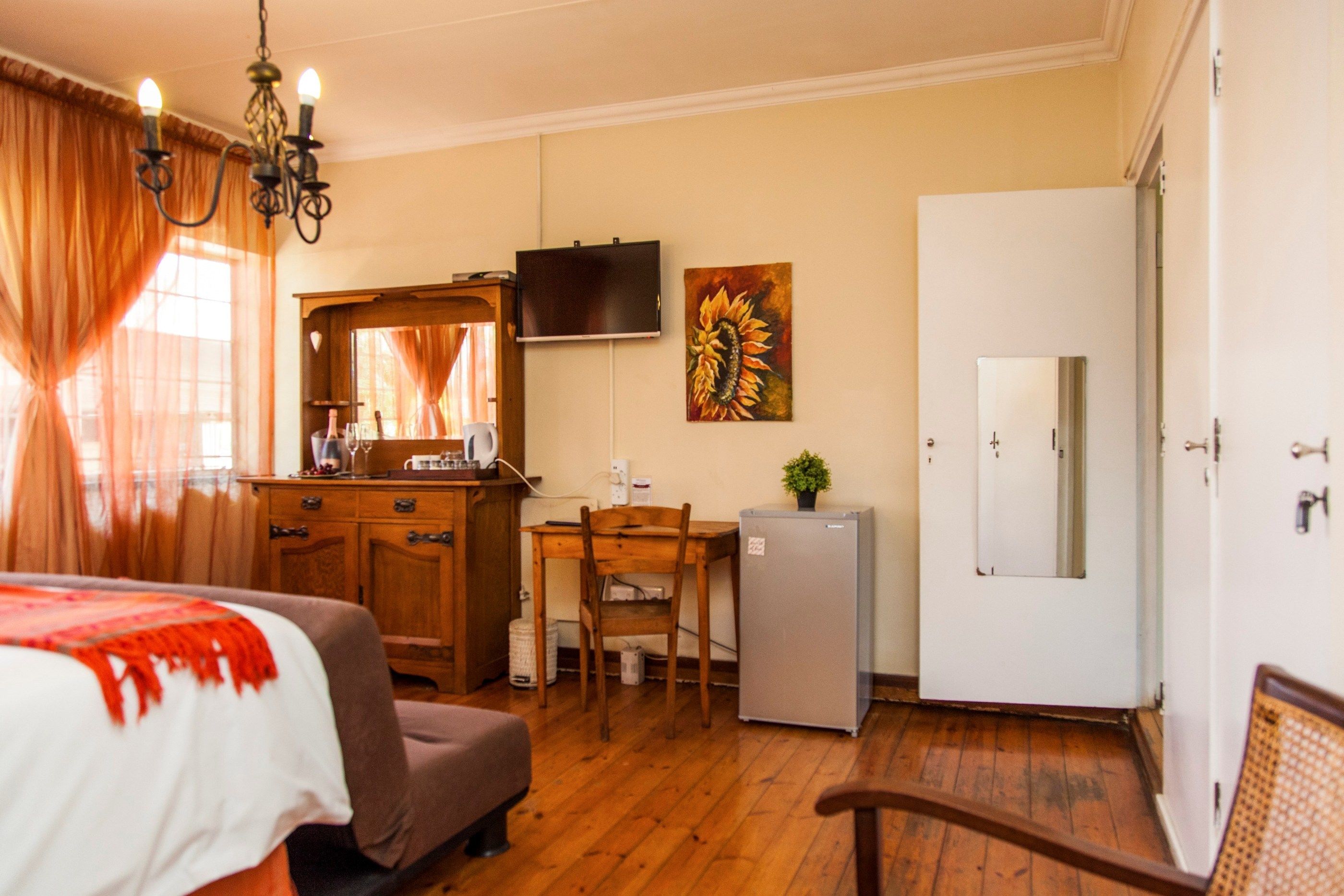 Quarto de hotel com cama, escrivaninha, cadeira, frigorífico, televisão e porta.