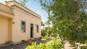 A two-story building with a beige facade, a small porch with potted plants, and a clear sky. - Casa Frulli (Uggiano la Chiesa)