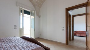 A bedroom with a large bed, a door leading to a balcony, and a view of a red bed in the adjacent room. - Casa Frulli (Uggiano la Chiesa)